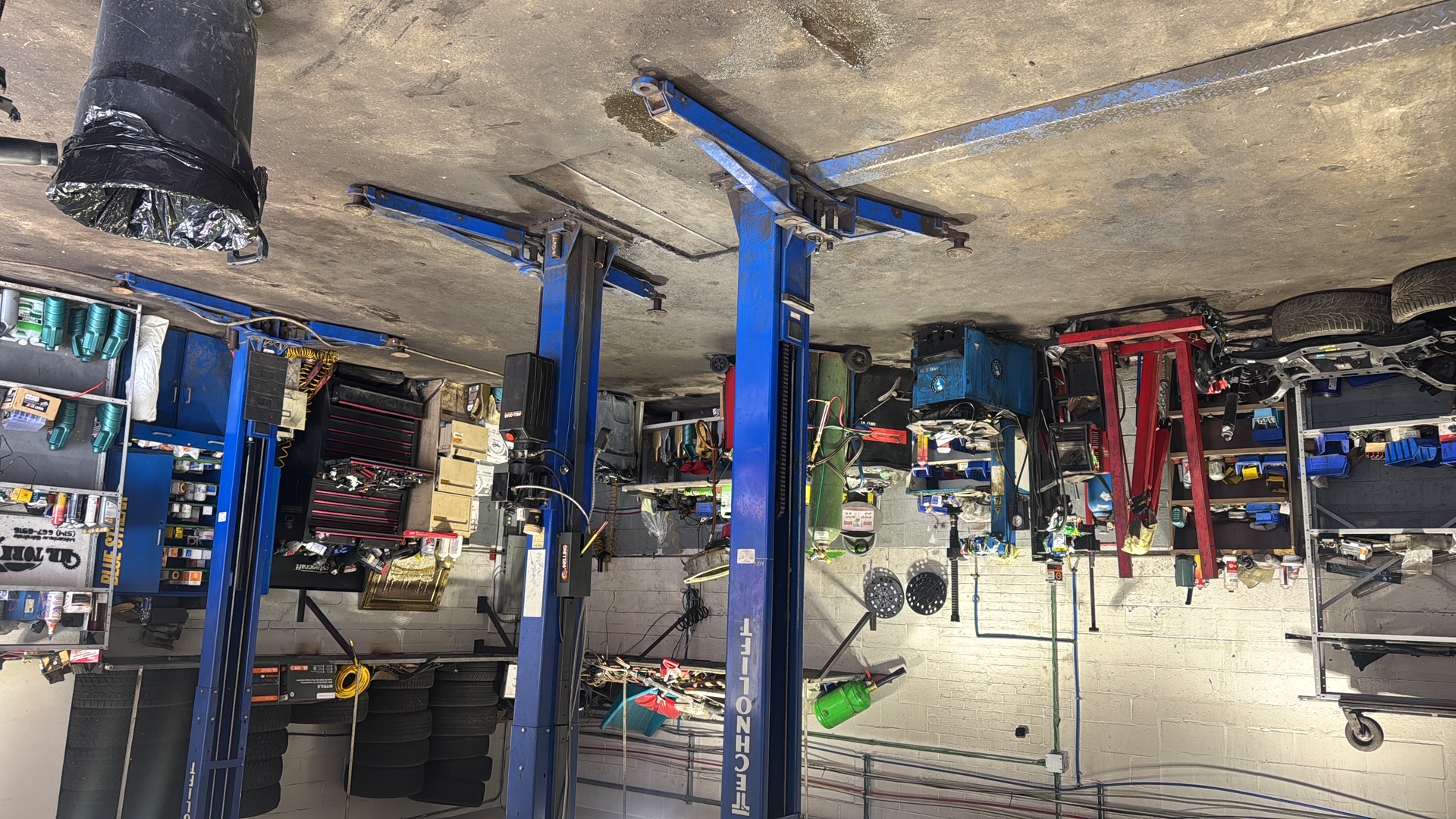 Inside the workshop, with blue hydraulic lifts, tools, and tire storage